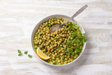 Stewed chickpeas in green sauce with parsley and lemon on a white wooden background, rustic style, top view. delicious healthy homemade food	