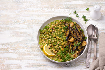 Stewed chickpeas in green sauce with with baked eggplant, parsley and lemon on white wooden background, rustic style, top view. delicious healthy homemade food