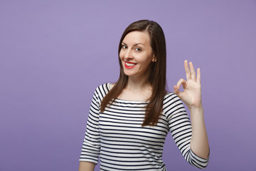 Young brunette woman girl in casual striped clothes posing isolated on violet purple background studio portrait. People sincere emotions lifestyle concept. Mock up copy space. Showing okay ok gesture.