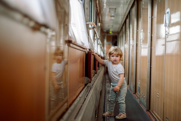 Fototapeta na wymiar Cute blonde baby girl plays on the train, travels in a compartment car, runs a long corridor. Travel concept with kids.