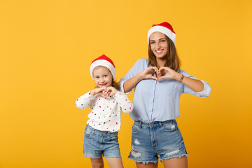 Fototapeta premium Woman child baby girl 4-5 years old in Christmas Santa hat. Mommy little kid daughter isolated on yellow background studio portrait. Happy New Year 2020 celebration holiday concept. Mock up copy space