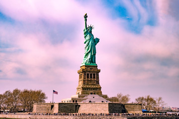 Statue of liberty with many tourists around it with pinky cloudy sky before sunset