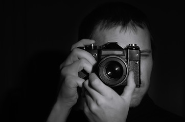 black and white portrait of a photographer with an old camera in his hands on a dark...