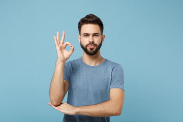Fototapeta premium Young attractive handsome man in casual clothes posing isolated on blue background, studio portrait. People sincere emotions lifestyle concept. Mock up copy space. Looking camera, showing OK gesture.