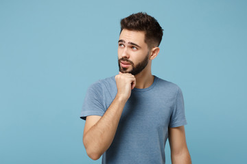 Young pensive man in casual clothes posing isolated on blue wall background, studio portrait. People sincere emotions lifestyle concept. Mock up copy space. Put hand prop up on chin, looking aside.