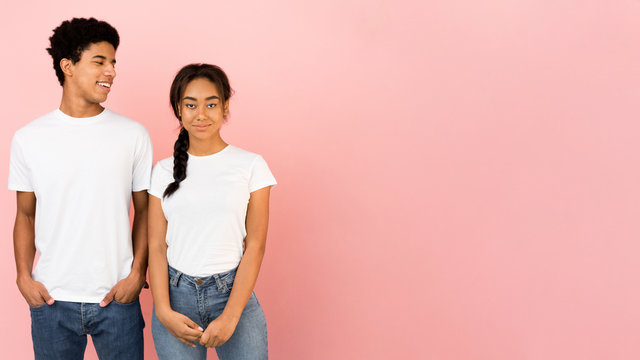 Young friends posing, guy looking at girl over pink background