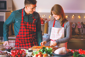 happy couple in aprons celebrating Christmas in the kitchen cooking christmas duck or Goose