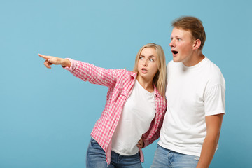 Young fun couple two friends guy girl in white pink empty blank design t-shirts posing isolated on pastel blue background studio portrait. People lifestyle concept. Mock up copy space. Looking aside.