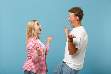 Young excited couple two friend guy girl in white pink blank design t-shirt posing isolated on pastel blue background. People lifestyle concept. Mock up copy space. Keeping mouth open spreading hands.