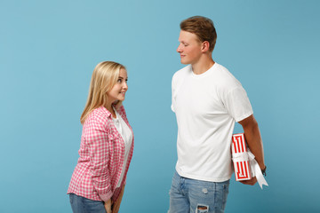 Young pretty couple two friends guy girl in white pink t-shirts posing isolated on blue background. Valentine's Day, Women's Day, birthday concept. Hold red striped present box with gift ribbon bow.