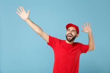 Delivery man in red uniform workwear isolated on blue wall background, studio portrait. Professional male employee in cap t-shirt print working as courier dealer. Service concept. Mock up copy space.