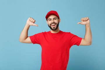 Fototapeta premium Delivery man in red uniform workwear isolated on blue wall background, studio portrait. Professional male employee in cap t-shirt print working as courier dealer. Service concept. Mock up copy space.