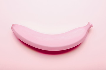 Painted pink banana on pink background, close up. Minimalism concept