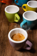 Various colored coffee cups and a cup with steaming espresso coffee
