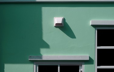 White dryer vent and part of window frames with sunlight and shadow on surface of pale green cement wall background of house building, home exterior architecture design concept