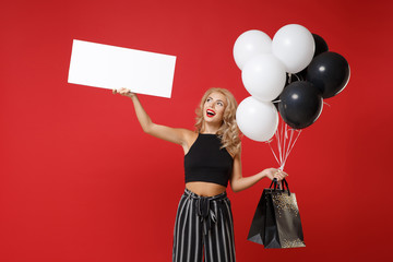 Funny woman girl in black clothes posing isolated on red background. Shopping discount sale concept. Mock up copy space. Hold air balloons package bag with purchases blank board with place for text.