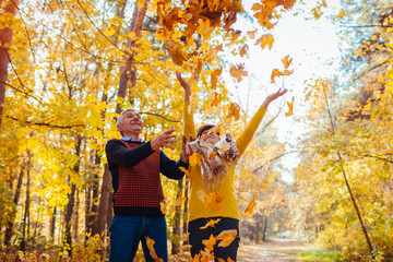 Fall season. Couple throwing leaves in autumn forest. Senior family having fun outdoors