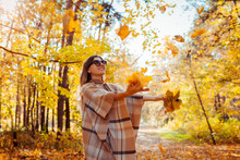 Fall season. Woman throwing leaves in autumn forest. Young woman having fun outdoors