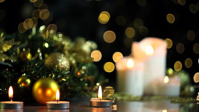 White candles are burning, decorated wreath, gold decor for christmas tree, balls are on table. Festive decorative garland, warm yellow light bulbs, lanterns are blinking on background. New year mood.