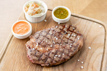 Sliced medium rare grilled Steak Ribeye with Pickled cabbage and two sauces. Serving on a wooden Board. Barbecue restaurant menu, a series of photos of different meats.