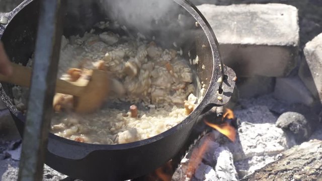 Cooking girolle (Cantharellus cibarius), Porcini (Boletus) mushroom and chicken risotto in cast iron pot on an open campfire