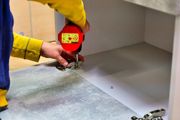 The worker makes, assembles a furniture cabinet from parts. Showing tools for work. The photo was taken in a really working manufactory.