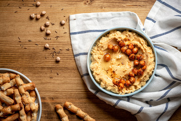 Hummus with olive oil and chickpeas in a ceramic plate on a wooden background, top view. Traditional middle eastern snack hummus, healthy vegetarian food.