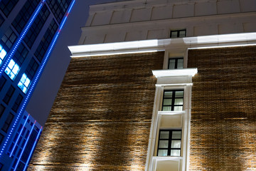 Part of the facade of a brick building with windows on the background of modern high-rise buildings at night