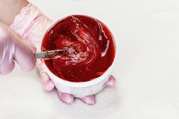 Beautician takes red transparent shugaring paste from a white can