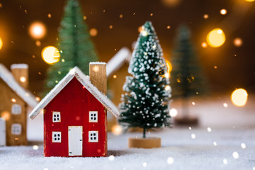 Miniature wooden houses on the snow over blurred Christmas decoration background, toned