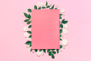 Flowers composition. Pink blank paper, white fresh roses and green leaves on gentle pink background. Flat lay, top view, copy space. Flower card, greeting, holiday mockup. Valentine's Day background