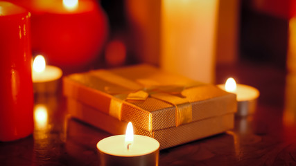 Closeup image of burning candles and golden small box with present for Christmas