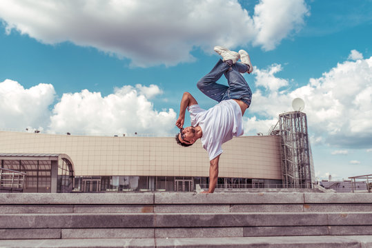 dancer on one arm dances break dance, hip-hop, artist acrobat. Summer city, clouds background. Active youth lifestyle, young male dancer, fitness movement workout breakdancer. Free space for text.