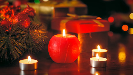 Closeup photo of red candle burning on wooden table decorated for Christmas
