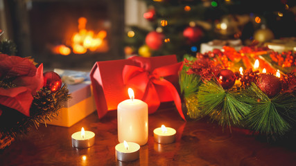 Beautiful image of Christmas wreath, burning candles and lantern against fire in fireplace