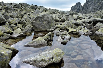 Lake in the mountains, big stones in the water against the background of cloudy sky.