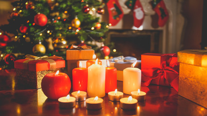 Beautiful toned image of burning candles and gifts from Santa against glowing decorated Christmas tree and fireplace at night
