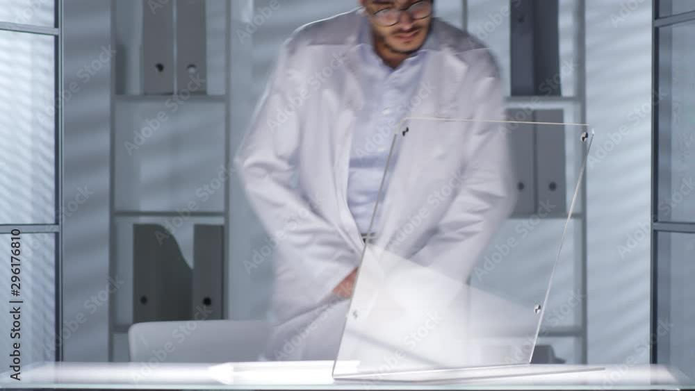 Poster middle eastern male doctor in lab coat turning on office desk lightning and typing on wireless futur