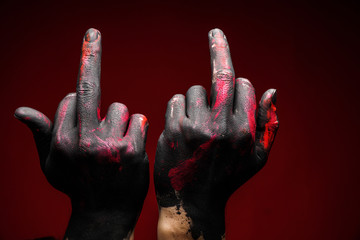 Two male hands in black, pink and red paint show middle finger on a dark background Close-up