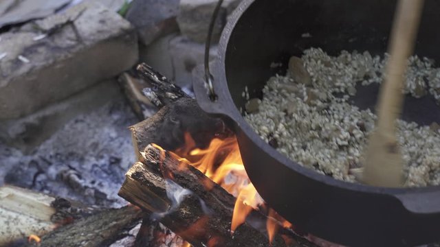 Cooking girolle (Cantharellus cibarius), Porcini (Boletus) mushroom and chicken risotto in cast iron pot on an open campfire