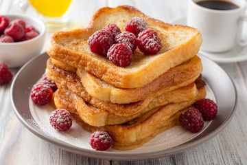 French toasts with powdered sugar and fresh raspberries on wooden table. Selective focus.