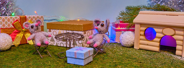 Fototapeta premium Two knitted rats sit at the table near the Christmas tree and gifts in the new year 2020. Symbol of 2020. Feast of the rat