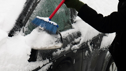  Scraping the snow of a car's wing mirror and side windows using the brush.