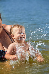 Fototapeta na wymiar Cute baby plays in the water in the arms of mom