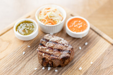 Fototapeta na wymiar Grilled fillet steaks with Pickled cabbage and two sauces. Serving on a wooden Board. Barbecue restaurant menu.