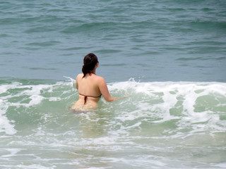 Fototapeta na wymiar Sea vacations, woman in swimsuit splashing in big waves, rear view. Concept of swimming, holidays and enjoying the water on paradise coast