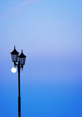 Design with silhouette of lamp post on blue and purple evening sky with moon., copy space