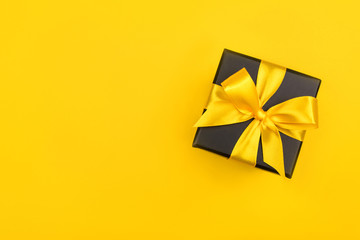Black gift box with bow on yellow background. Flat lay. Copy space.