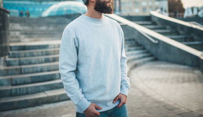 City portrait of handsome hipster guy with beard wearing gray blank hoodie or hoody and hat with...