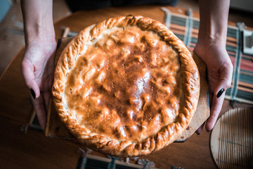 female hands hold a fresh hot apple pie in the kitchen. made with your own hands